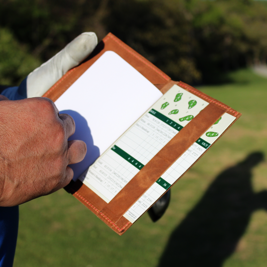 Person holding a golf scorecard with a green field in the background