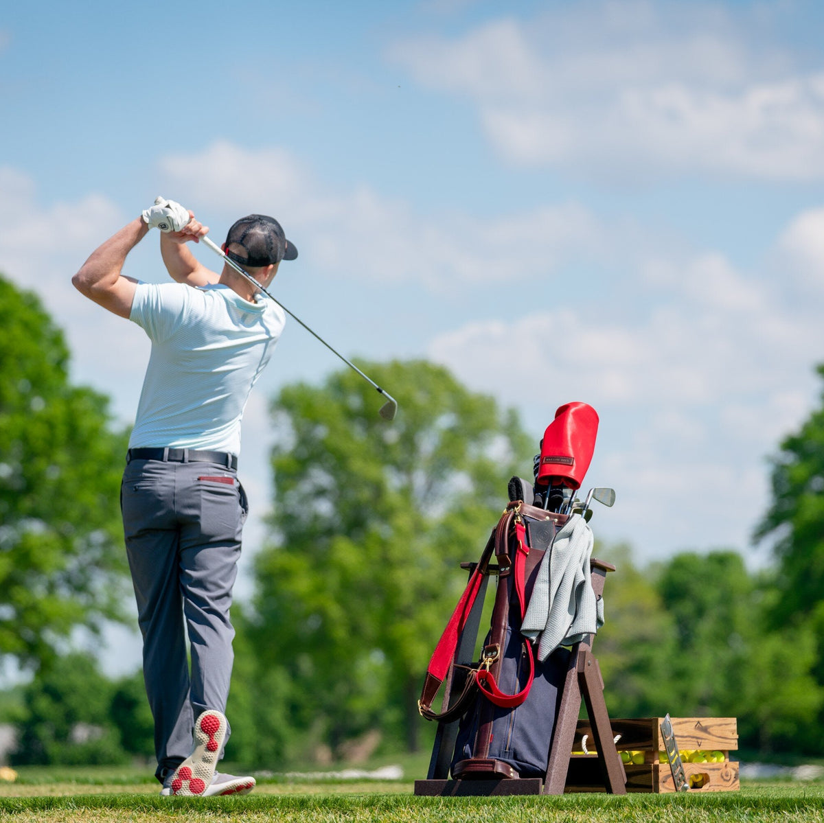 Man practicing golf swings on a driving range with trees and clear sky in the background.