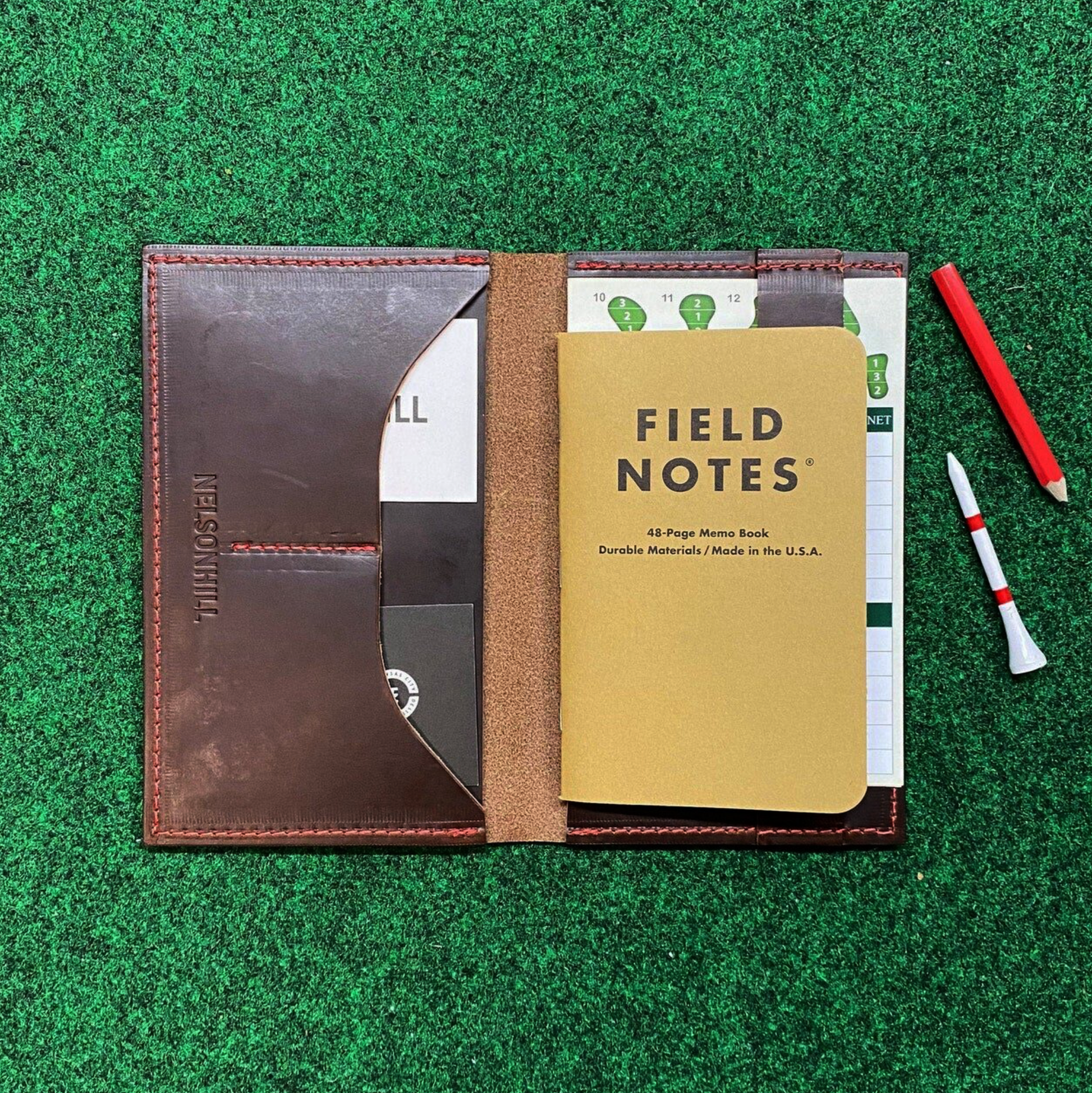 Brown leather wallet with a Field Notes notebook on green grass