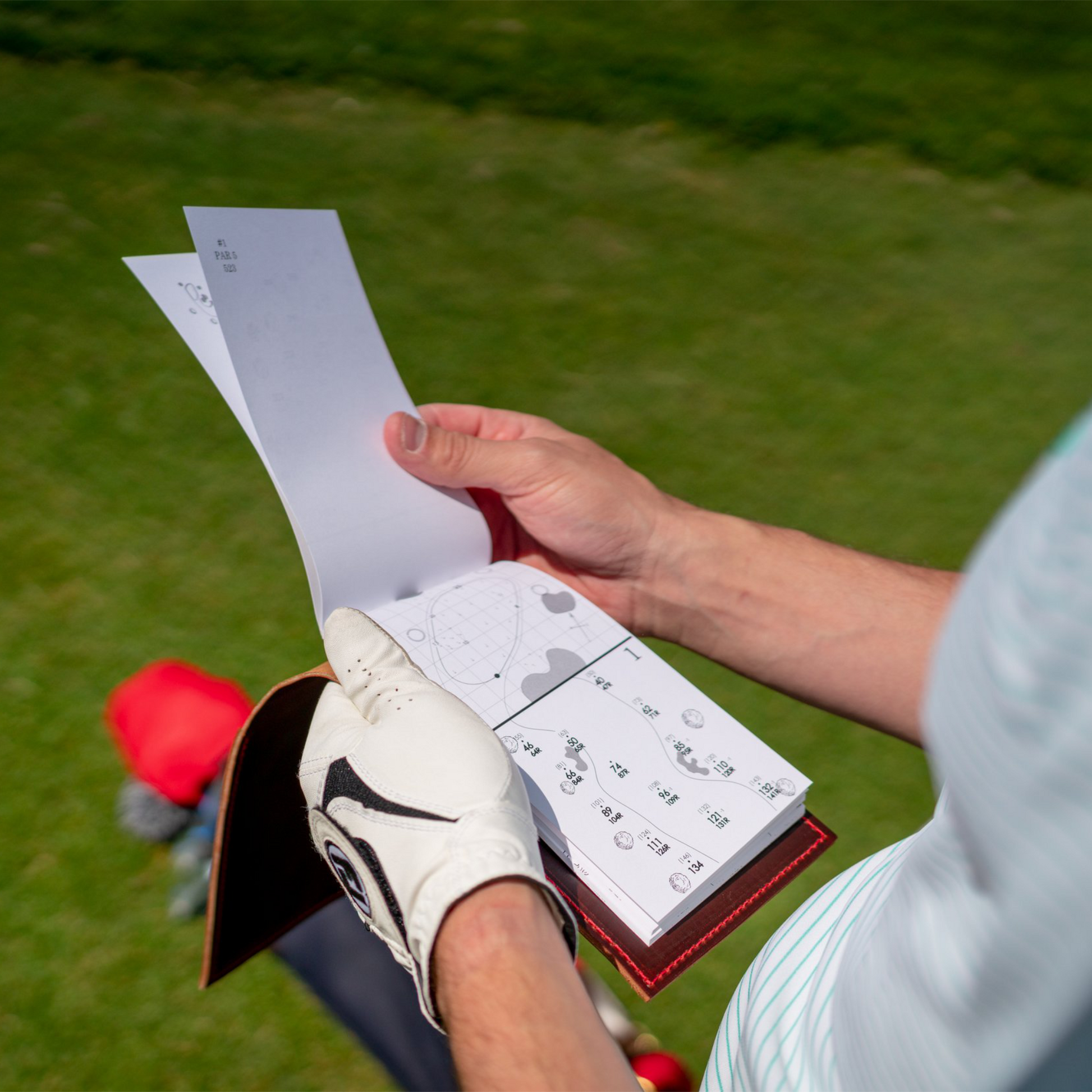 Golfer holding a yardage book and leather cover on a golf course.
