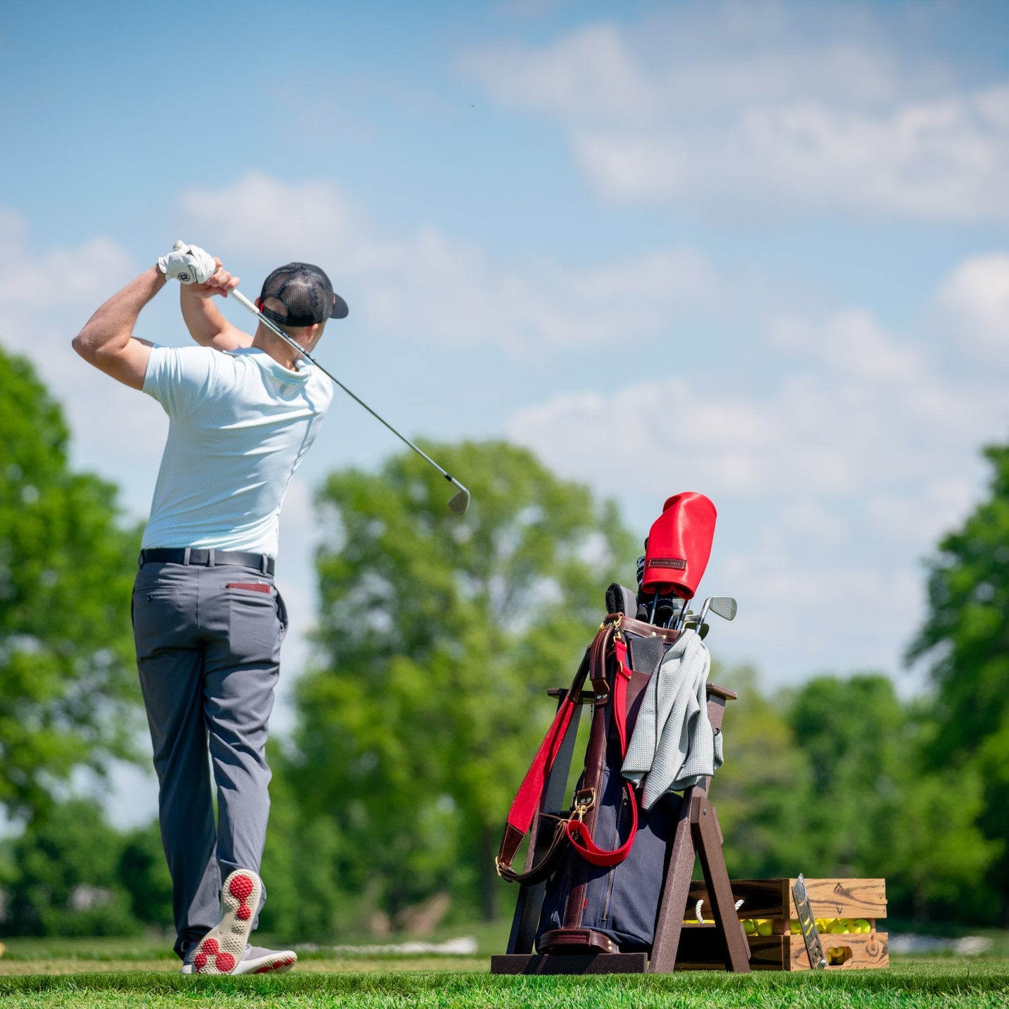 Golfer on a golf driving range with a golf bag and clubs in the foreground.