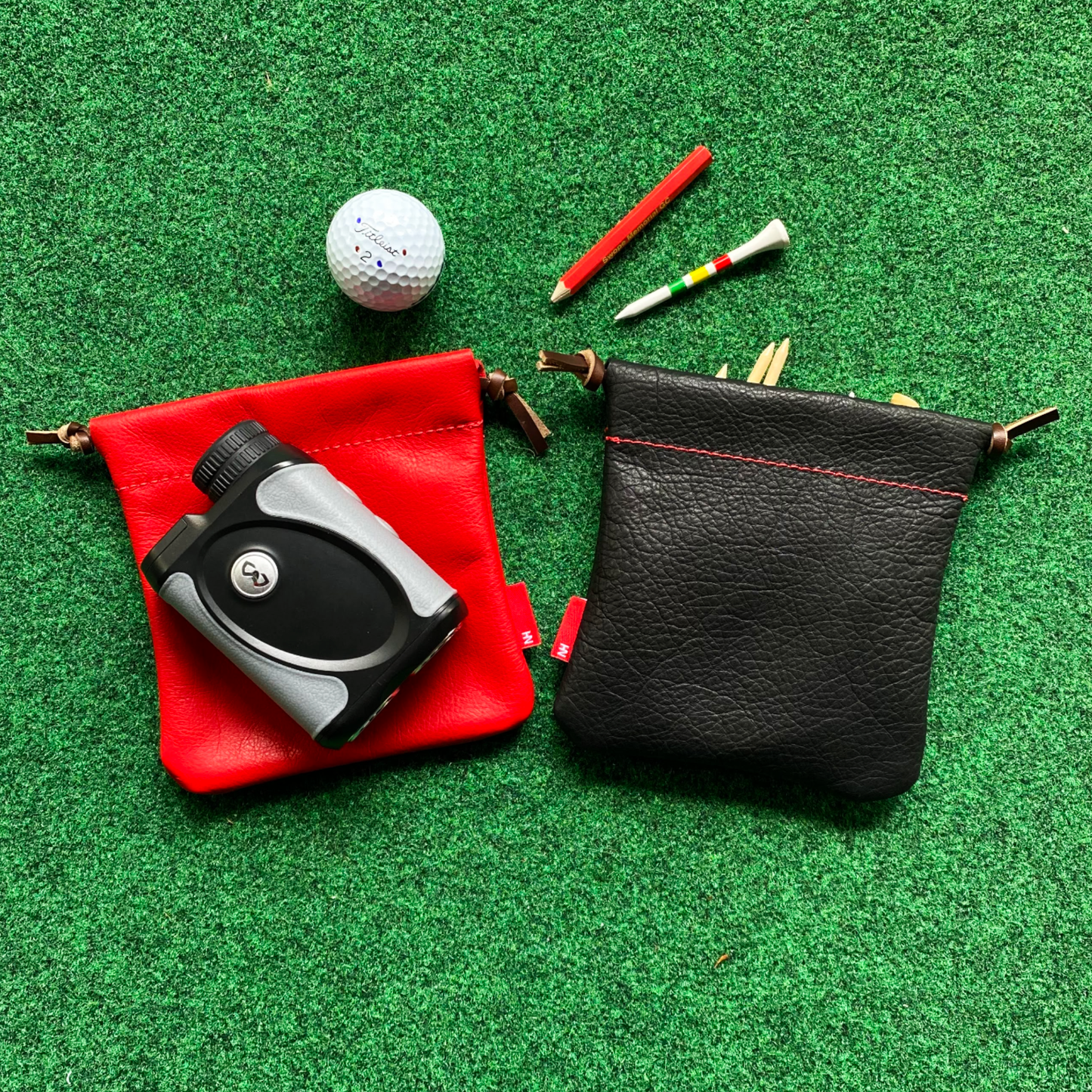 Golf accessories including a golf ball, putters, and a black pouch on a green surface.
