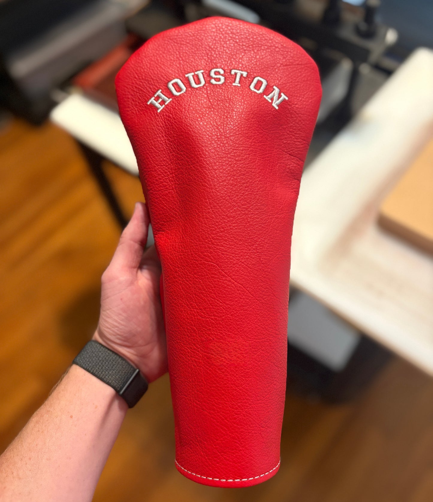 Red golf club head cover with 'Houston' branding held by a person indoors.