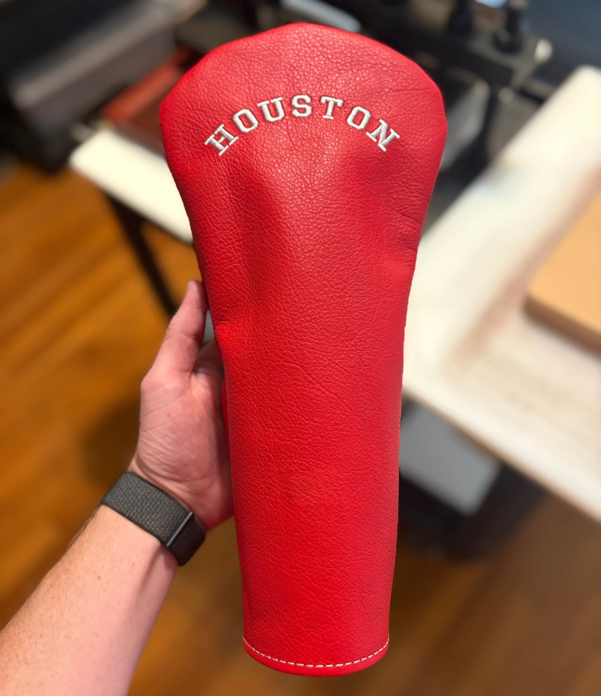 Red golf club head cover with 'Houston' branding held by a person indoors.