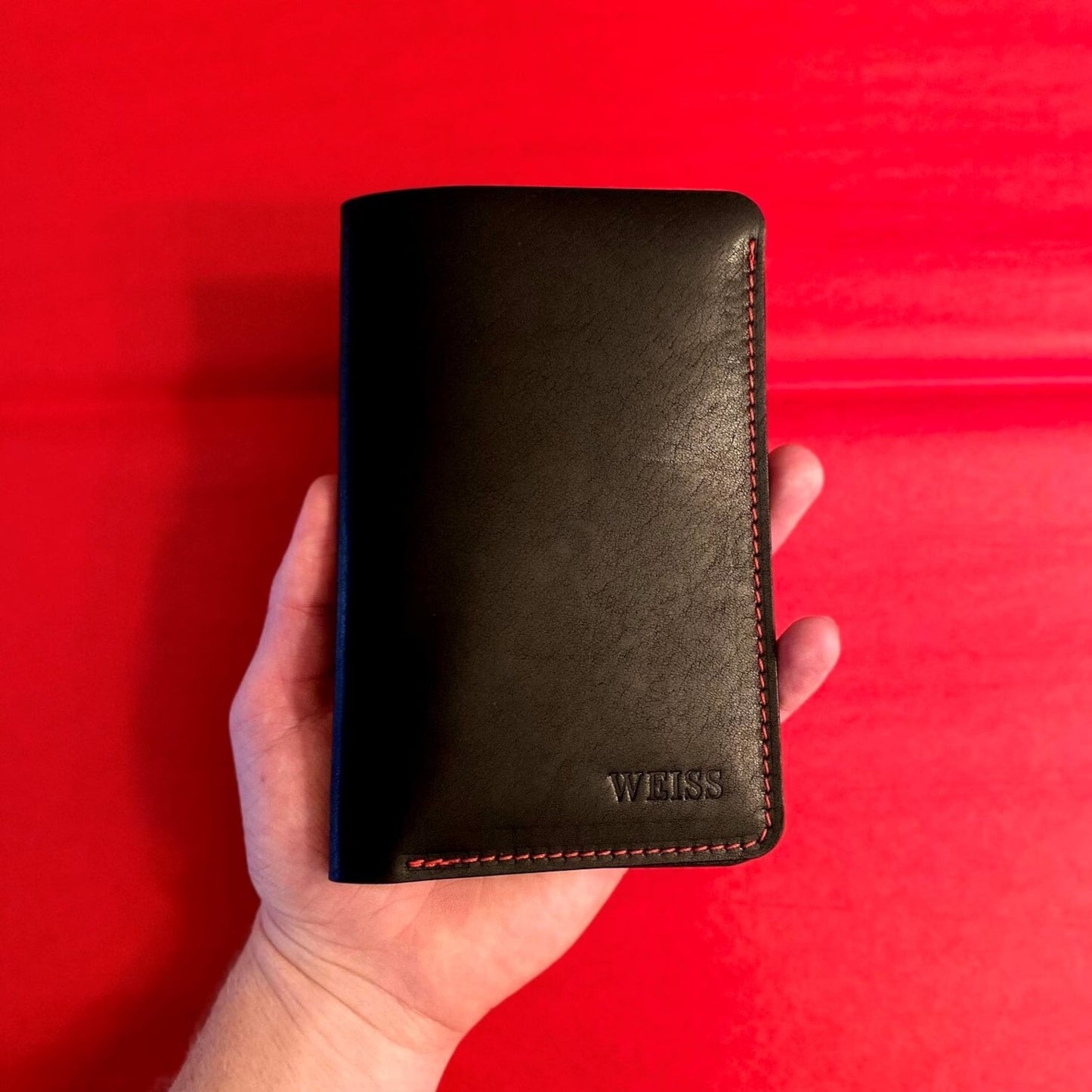 Hand holding a black golf scorecard holder against a red background