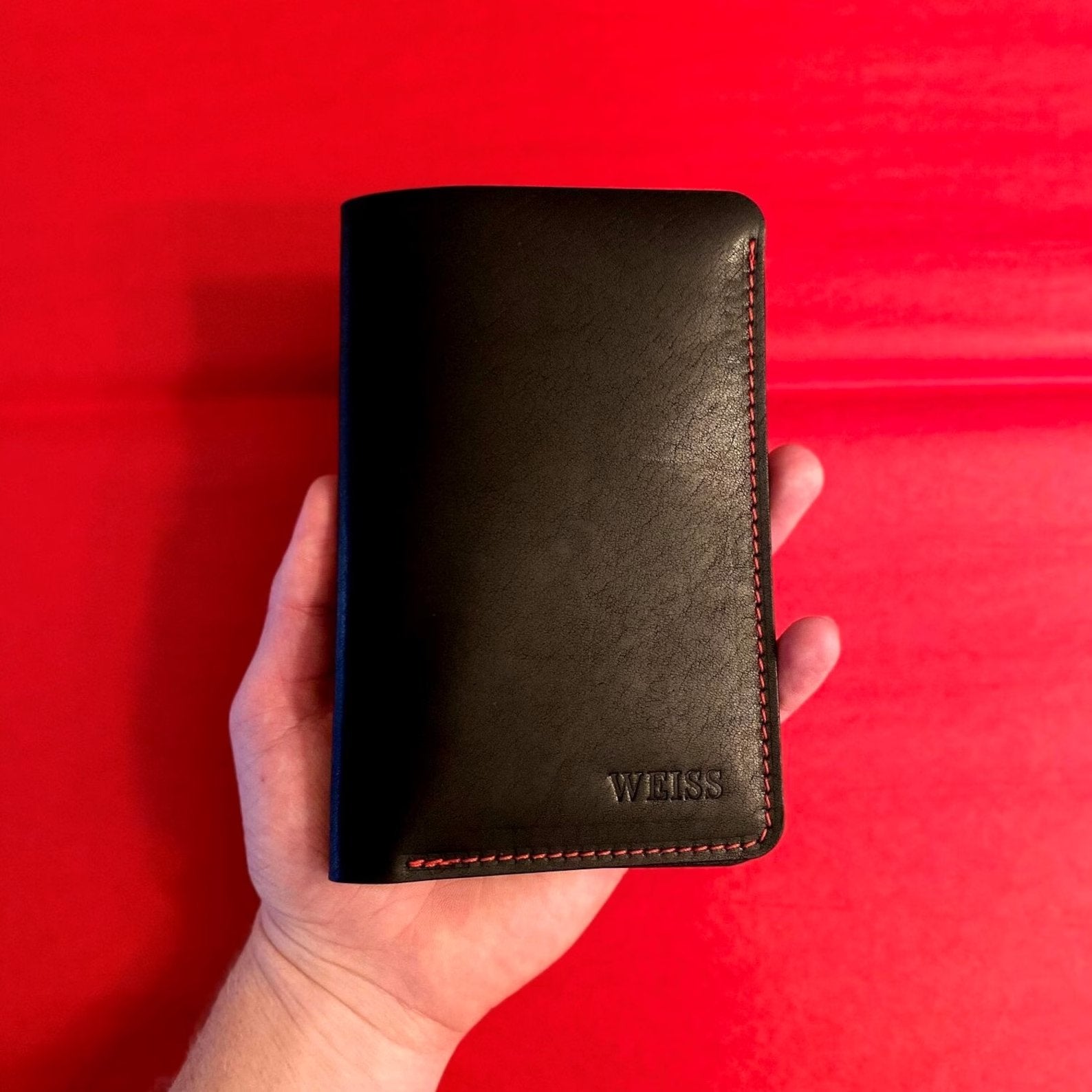 Hand holding a black golf scorecard holder against a red background