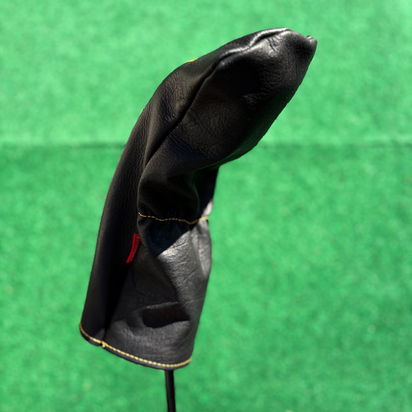 Black golf club head cover on a green background