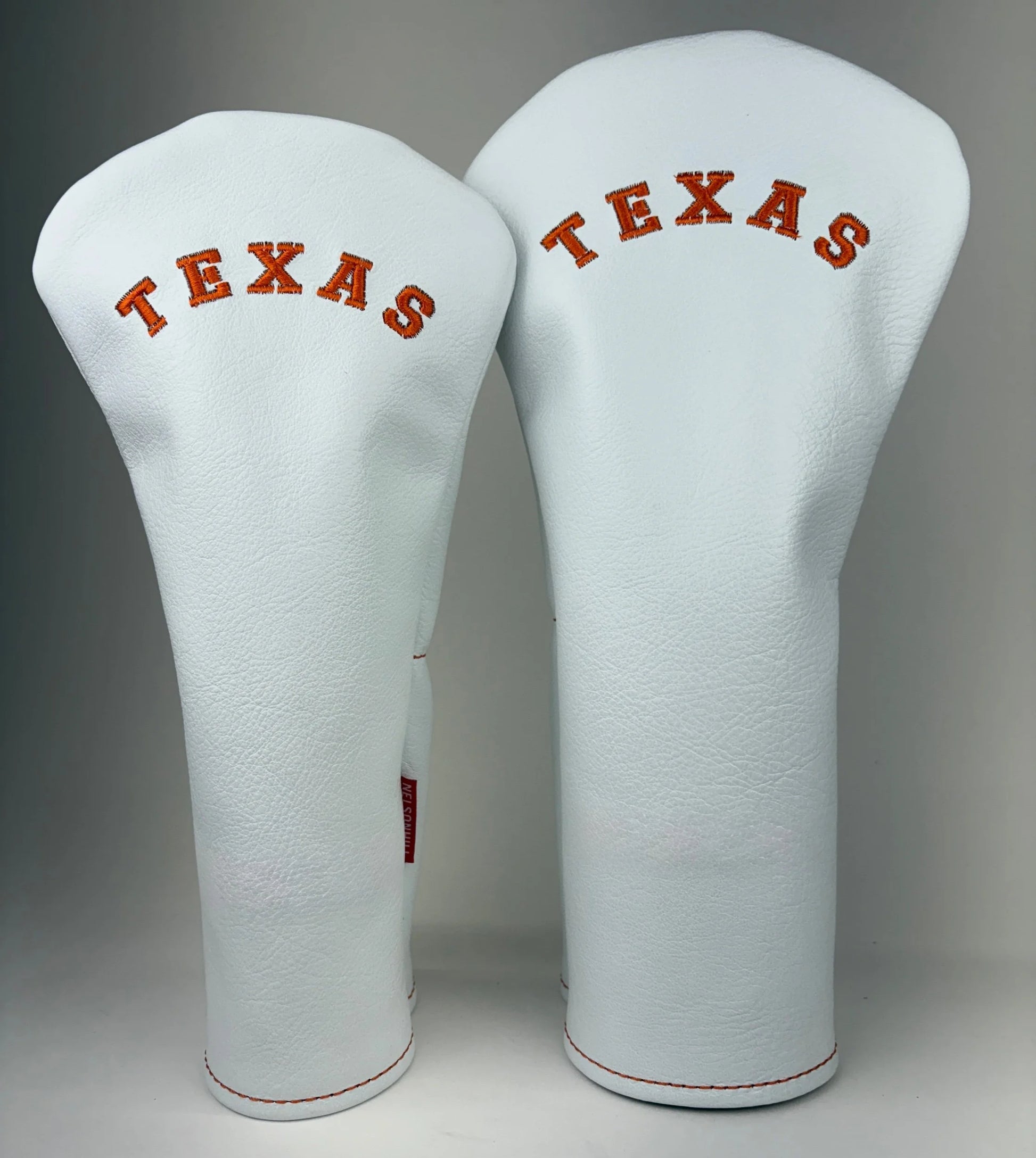 Two white golf club head covers with 'TEXAS' text on a gray background
