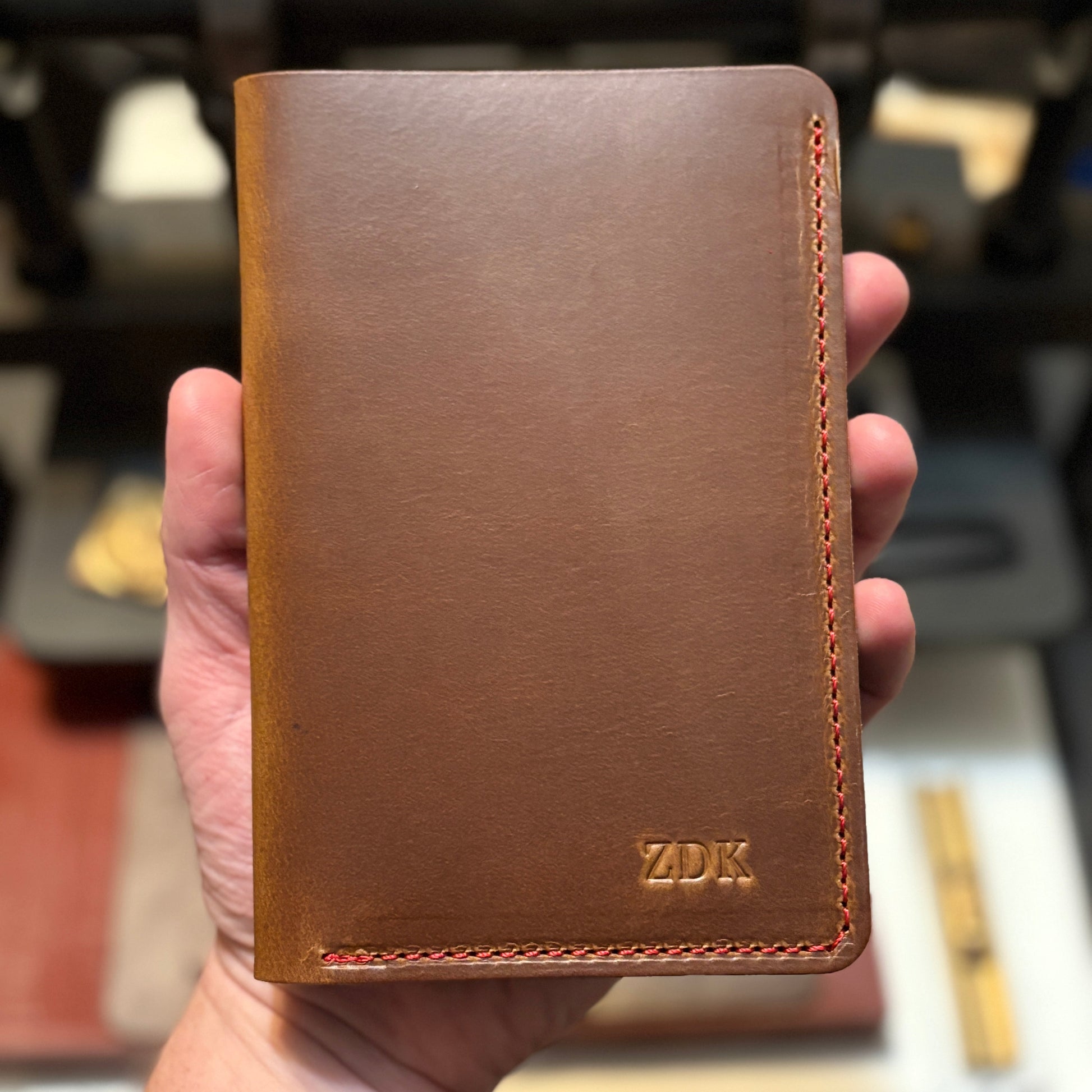 Caramel leather scorecard wallet held in a hand with a blurred background
