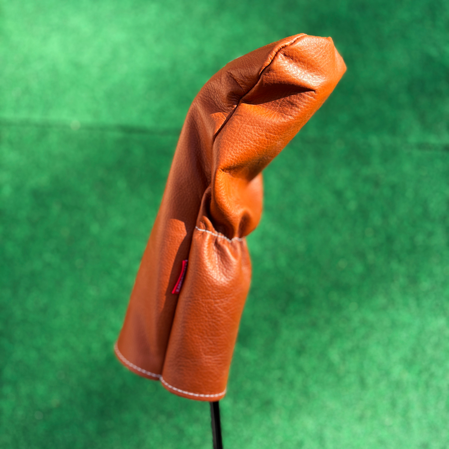 Brown leather golf club head cover on a green background