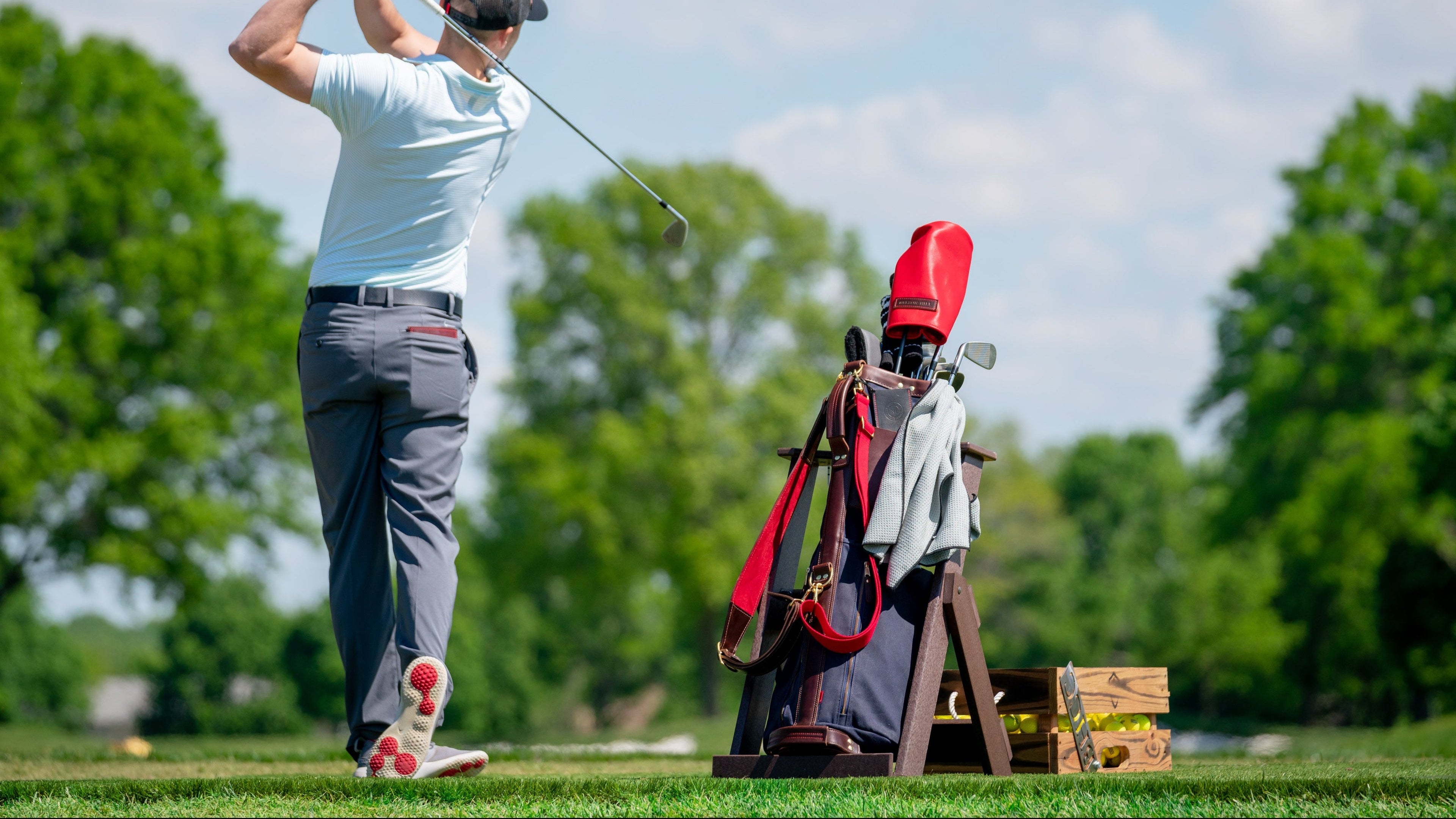 Golfer in action on a golf course with a golf bag and clubs in the foreground.