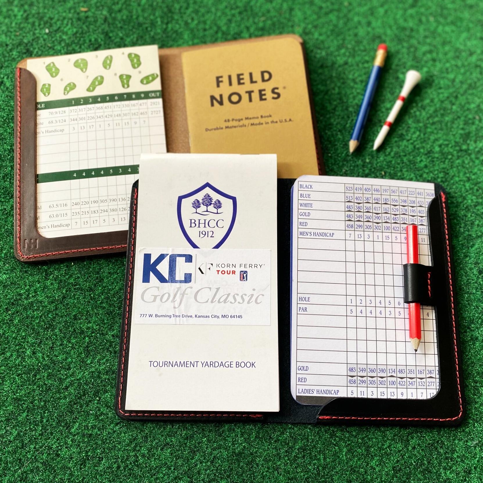 Golf scorecard holders with a scorecard, notebook, and yardage book on a green surface